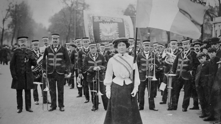 Une suffragette portant un drapeau devant un groupe d'hommes